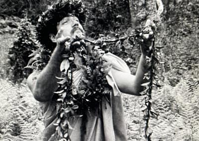 Native Hawaiian cultural practitioner in the forest holding up a lei offering.